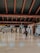A spacious airport terminal with a polished floor and high ceiling supported by large beams. Overhead signs provide directions to various airport facilities such as departure gates and medical assistance. Few travelers are present, including one person walking with luggage.