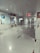 A clean, empty hallway with glossy tiled flooring and white walls. Overhead, there is a ceiling with recessed lighting, and on the right side, a series of doors and signs are visible. There is a television mounted on the wall and some signage indicating directions or information.