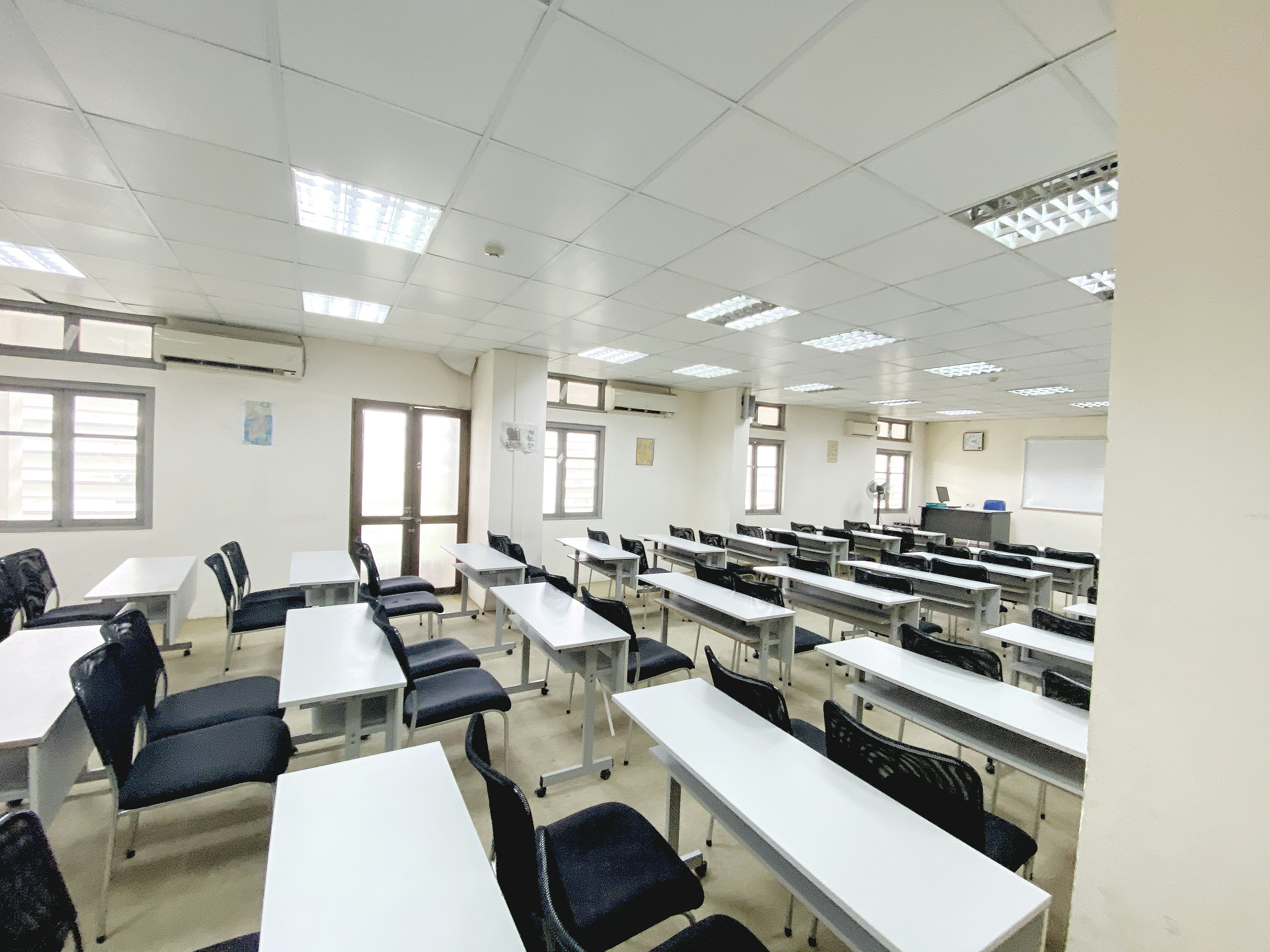 Accessible adult education classroom with desks arranged in rows, bright overhead lighting, whiteboards and educational materials on walls