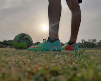a person's legs and feet on a football ball in a field
