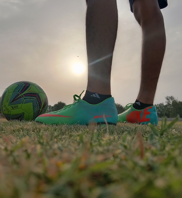 a person's legs and feet on a football ball in a field