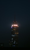 A tall, illuminated skyscraper stands against a dark night sky. A digital clock displaying the time 6:32:01 is prominently lit at the top. The building is structured with multiple floors, each with lights, and the word 'LATINOAMERICANA' is visible below the clock.
