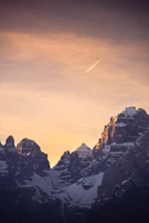 A private jet soaring above snow-capped mountains in golden hour light.