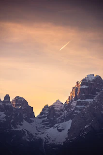 A private jet soaring above snow-capped mountains in golden hour light.