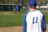 A smiling young baseball player in a navy jersey throwing a ball on a sunny field.
