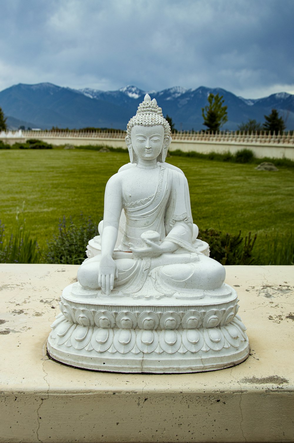 a statue of a person sitting on a rock in front of a field