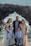 A family of five stands together posing for a photo with a rocky coastal background. The family consists of two adults and three children dressed in formal attire, standing on a cliff with waves crashing against the rocks behind them.
