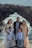 A family of five stands together posing for a photo with a rocky coastal background. The family consists of two adults and three children dressed in formal attire, standing on a cliff with waves crashing against the rocks behind them.