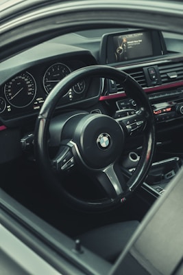 A detailed view of a car interior featuring a steering wheel with a prominent logo, dashboard gauges, a central control panel, and a display screen with navigational information.