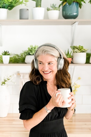 A smiling woman sitting peacefully with headphones on, surrounded by plants.