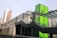 A modern urban structure with a prominent green panel featuring the letter 'G'. The building includes sleek glass and metal architectural elements. In the background, a multi-story residential building is visible under a clear sky.