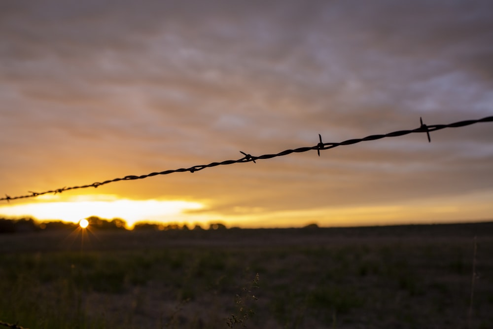 Una cerca de alambre de púas con una puesta de sol en el fondo