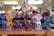 A collection of vividly colored, handcrafted cat figurines arranged on a wooden shelf. Each figure features bright patterns and designs that include stars and dots in multiple colors. The background is softly blurred, suggesting a shop or display setting.
