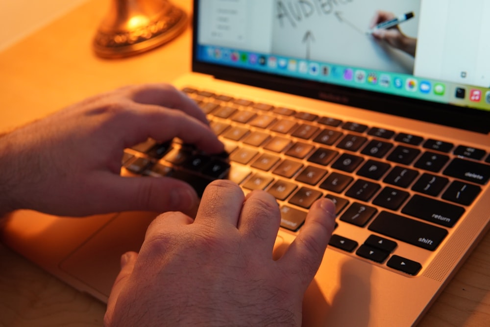 un par de manos escribiendo en el teclado de una computadora portátil