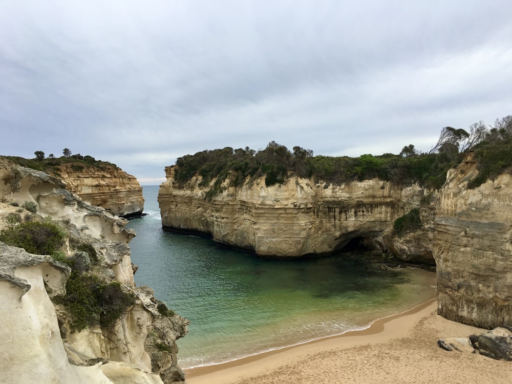 a beach with a cliff and water with Loch Ard Gorge in the background