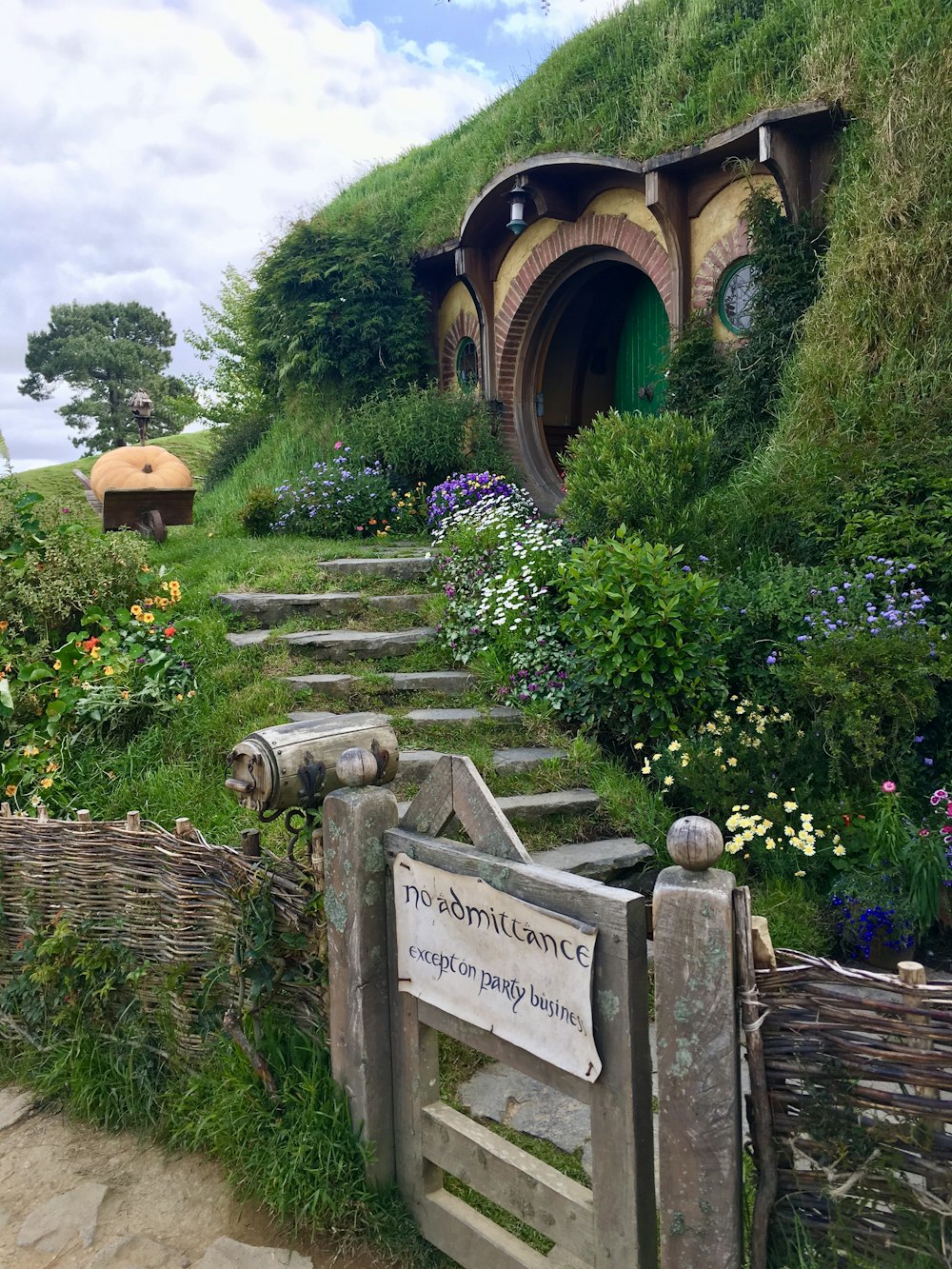 a stone walkway with a sign on it and a stone wall with plants and trees and a building