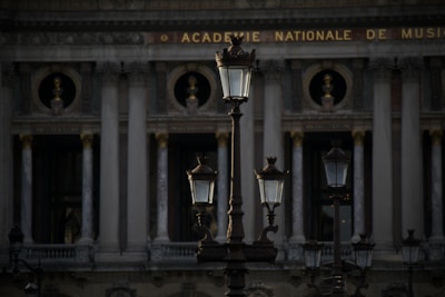 Several ornate street lamps stand in front of a classical building with tall columns and decorative sculptures. The architecture indicates a historic style with a focus on grandeur and symmetry. The building has the phrase 'Academie Nationale de Musique' inscribed at the top.