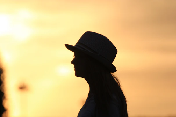 A sunset silhouette of a person wearing a floppy hat, capturing the essence of a warm summer evening.