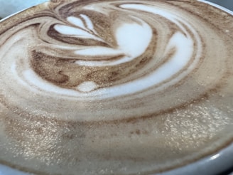 A close-up view of a cup of coffee with intricate latte art featuring swirling patterns of creamy white frothed milk blended with rich brown coffee.