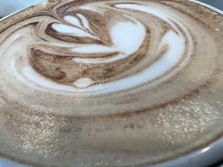 A close-up view of a cup of coffee with intricate latte art featuring swirling patterns of creamy white frothed milk blended with rich brown coffee.