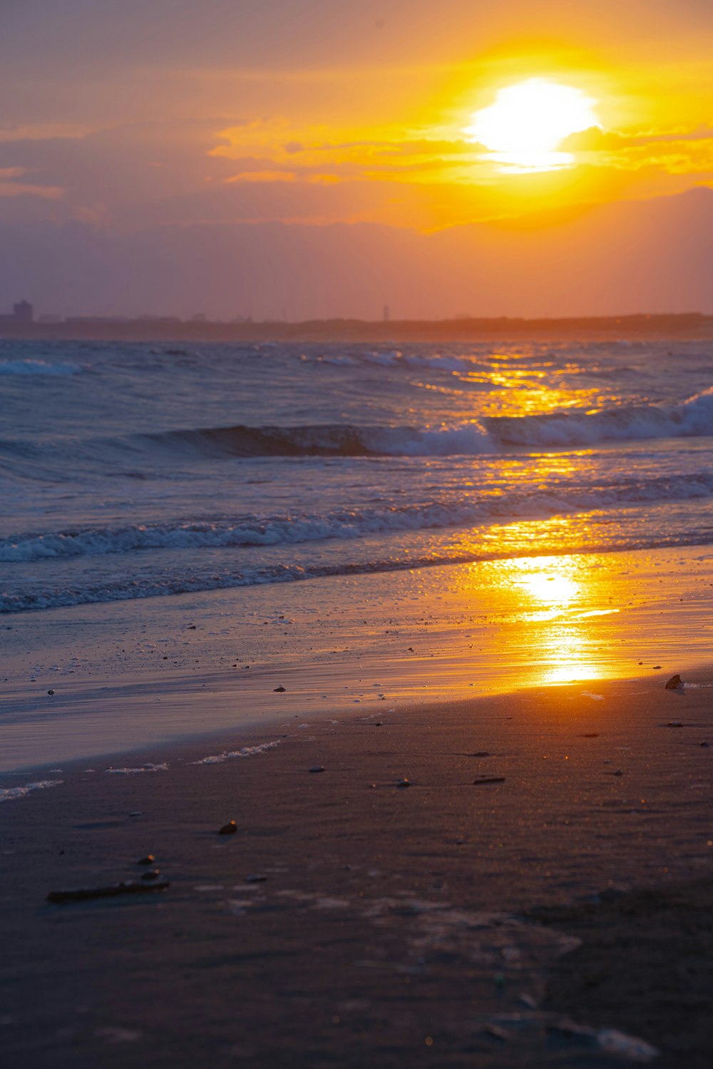 a beach with waves and the sun setting