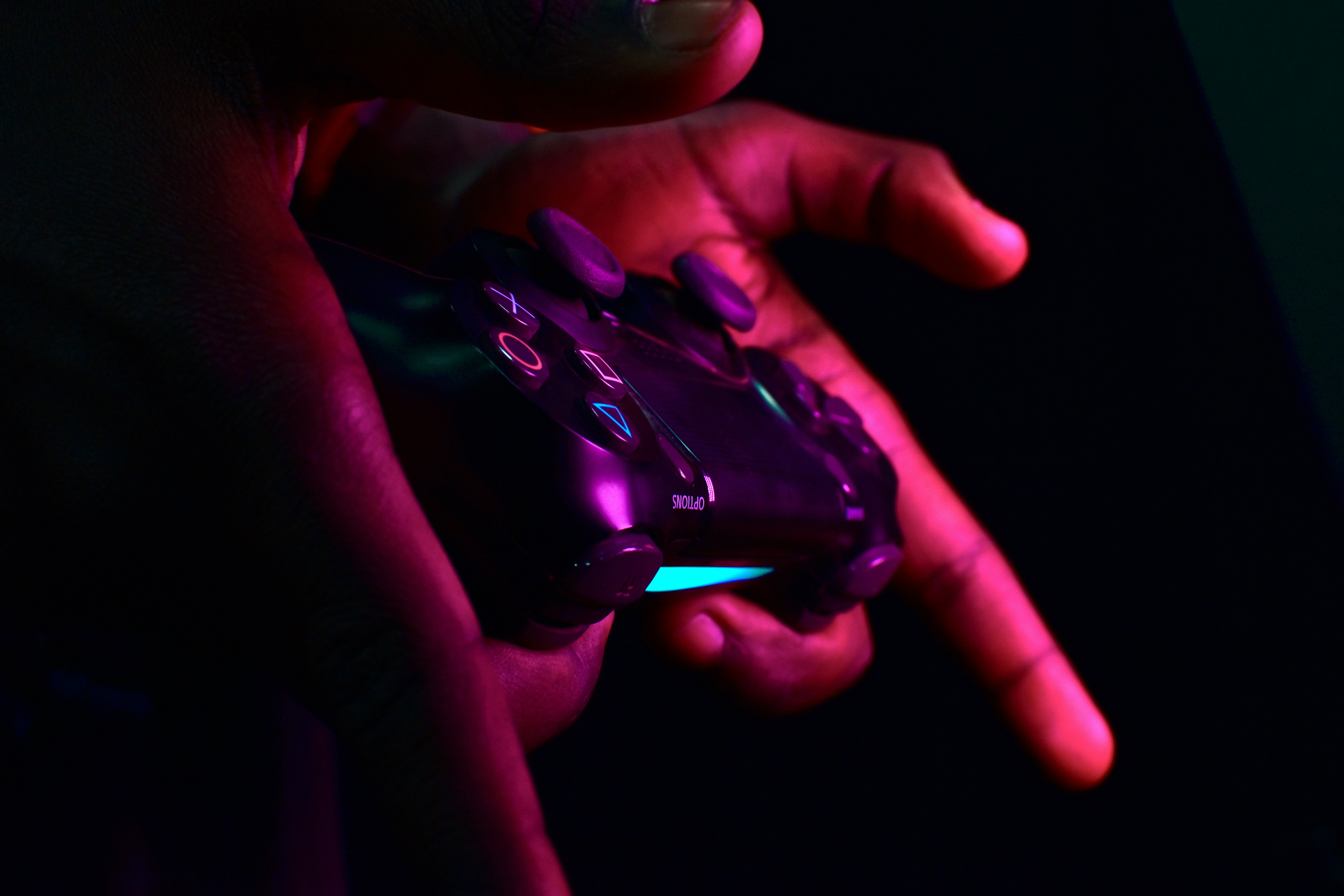 Manos negras sujetando un mando de videojuegos con luces de colores.