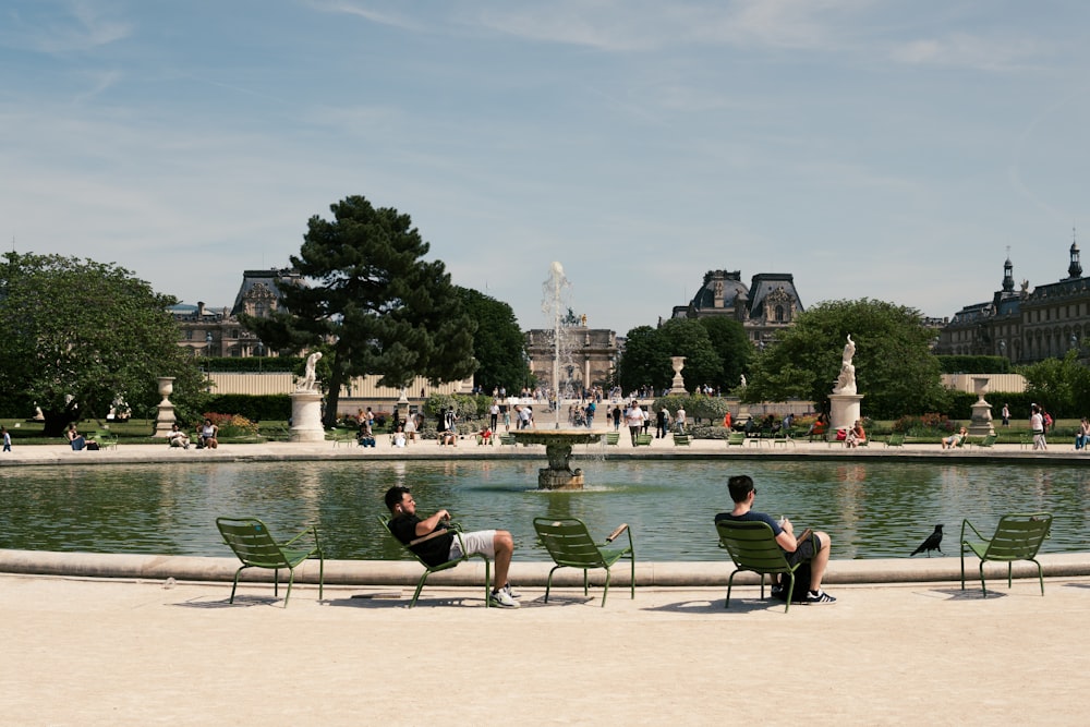 a couple of men sitting on green chairs in front of a fountain