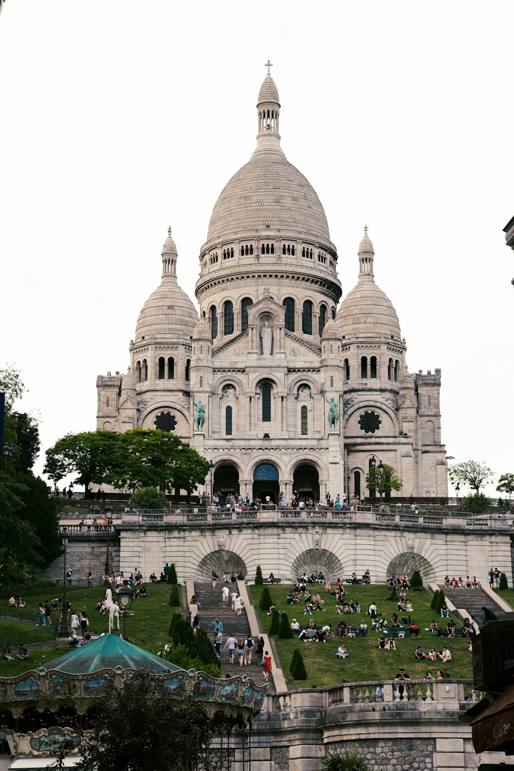 돔이 있는 커다란 흰색 건물과 파리의 사크레쾨르(Sacré-Cœur)를 배경으로 많은 사람들이 앞에 있습니다.
