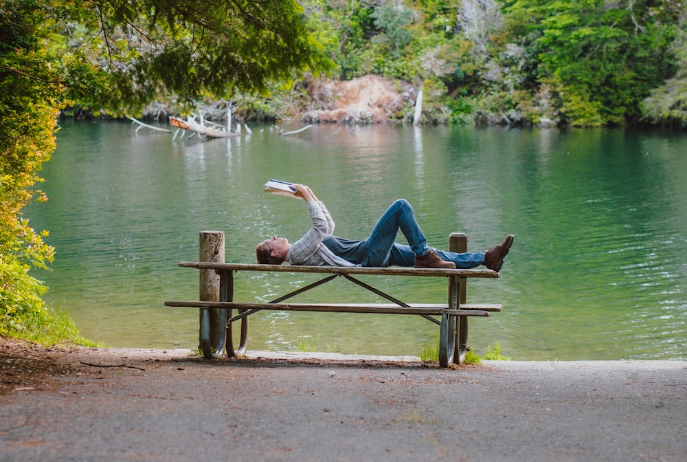 a person lying on a bench by a lake