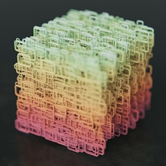 A complex, three-dimensional cube-shaped structure composed of interconnected, wireframe-like rectangular shapes. The structure features a gradient color scheme transitioning from shades of green at the top to yellow and pink at the bottom, set against a dark background.