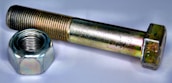 A metallic bolt and nut are placed on a white surface. The bolt has a hexagonal head and is positioned parallel to the nut, which is similarly hexagonal and threaded. Both objects have a shiny metallic surface with slight colorful reflections due to the lighting.