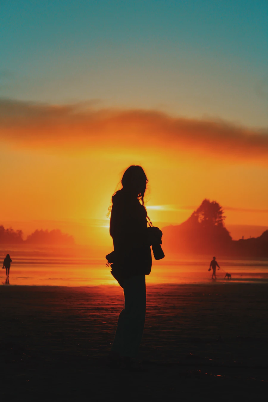 A lone person standing on the broad golden sands of a Tofino beach with the Pacific stretching behind them