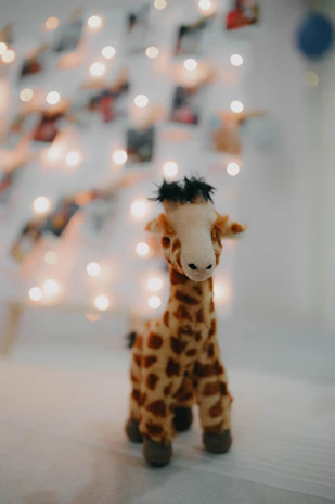 Close-up of a smiling giraffe toy wearing a tiny knitted scarf against a cream background.