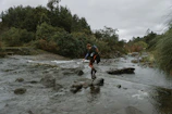 Hiker crossing a stream in a breathable ultra-lite rain shell with a backpack.