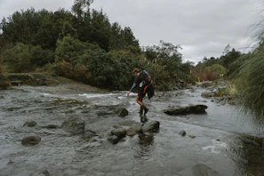 Hiker crossing a stream in a breathable ultra-lite rain shell with a backpack.
