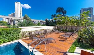 a pool with chairs and tables by it and buildings in the background