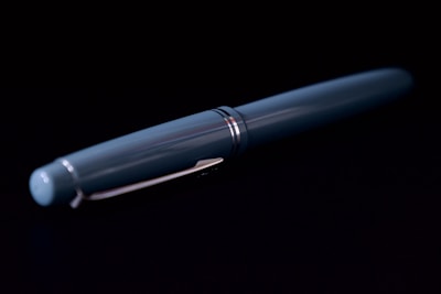 A sleek, dark blue fountain pen is displayed against a black background. The pen has metallic accents and a glossy finish, emphasizing its elegant design.