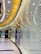 A brightly lit luxury store interior, featuring sleek, curving architecture and glossy surfaces. The walls have a reflective quality with patterned designs, and there are prominent brand logos displayed on the exterior. The color palette consists of warm gold tones complemented by neutral grays and blacks.