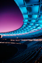 A futuristic stadium bathed in blue and purple neon under a night sky.