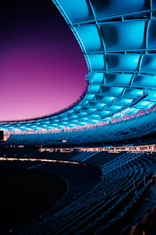 A futuristic stadium bathed in blue and purple neon under a night sky.