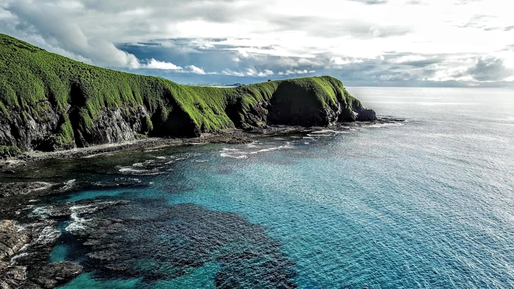 a body of water with a rocky shoreline and green hills in the background