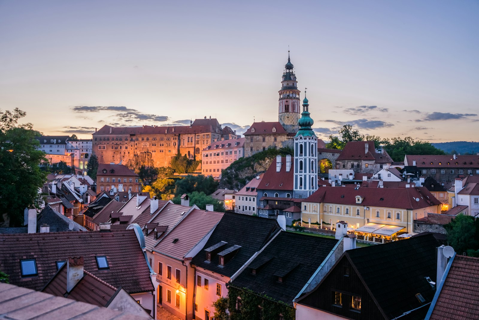 Twilight view of Český Krumlov with the illuminated castle tower above red-tiled rooftops
