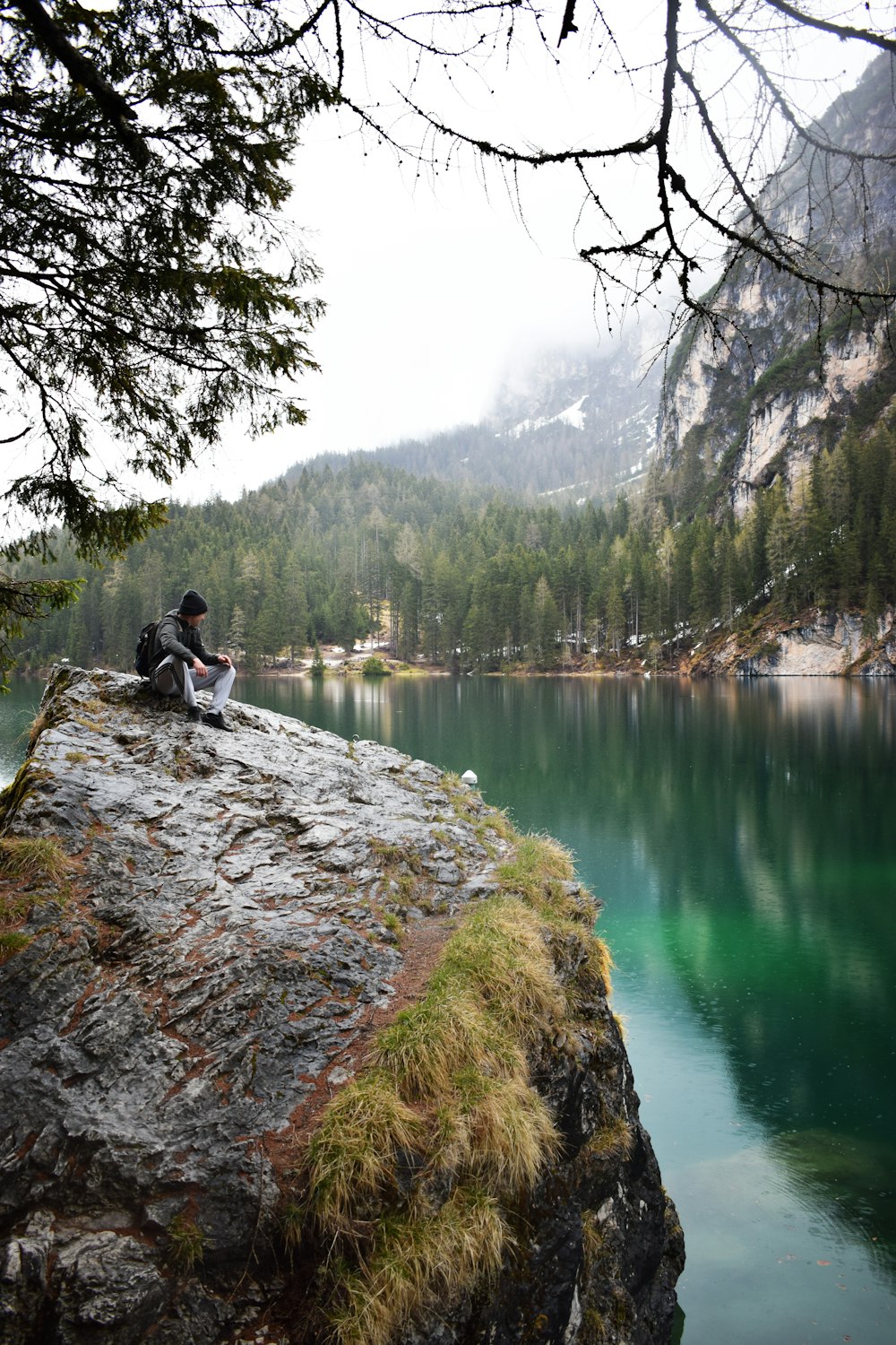 a person sitting on a rock by a lake with trees and mountains in the background