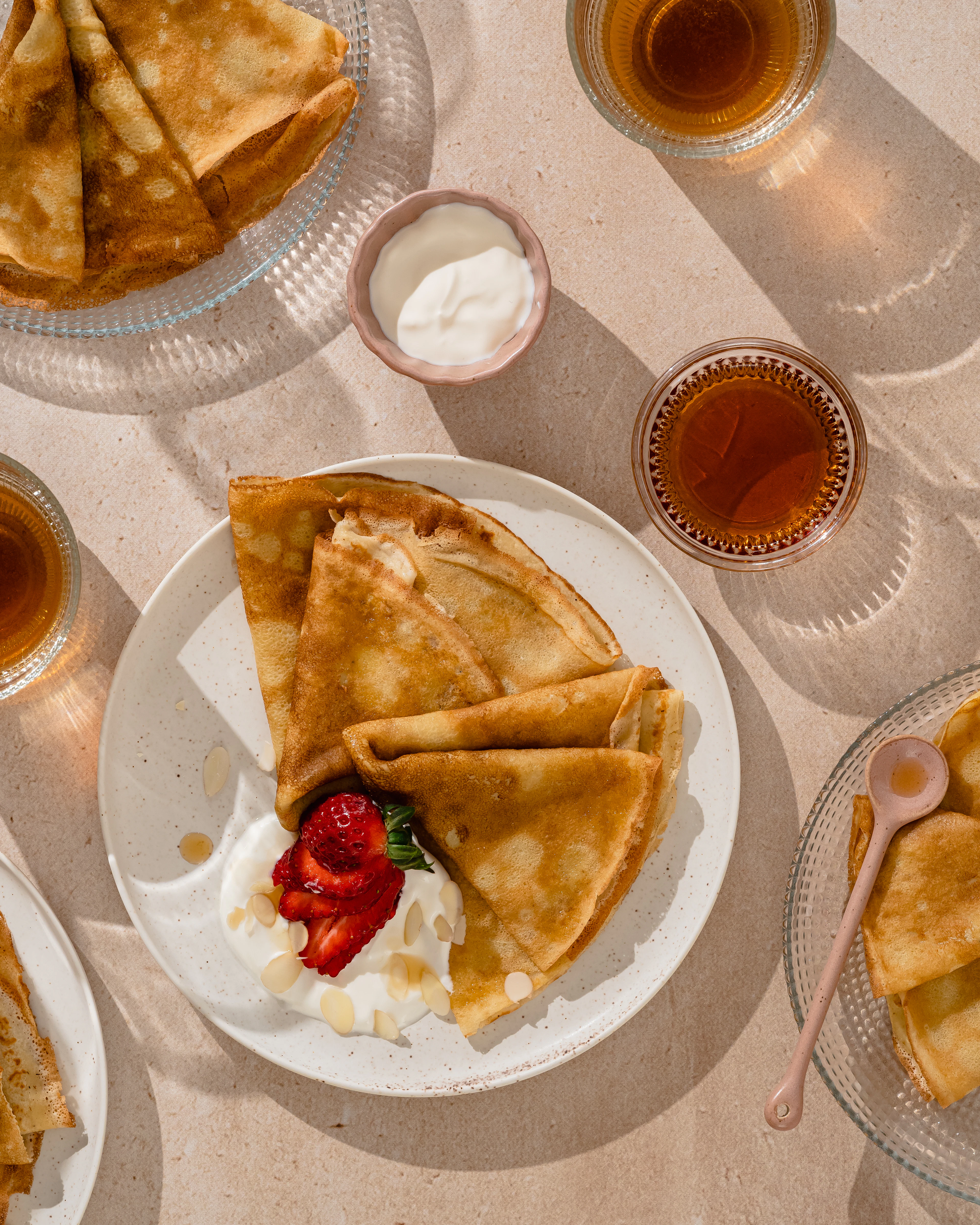 Folded crêpes on a plate with strawberries and cream, beside cups of tea