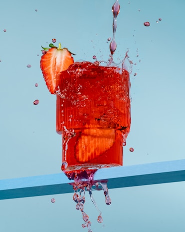 A vibrant splash of strawberry juice swirling around a Noorix strawberry energy drink can.