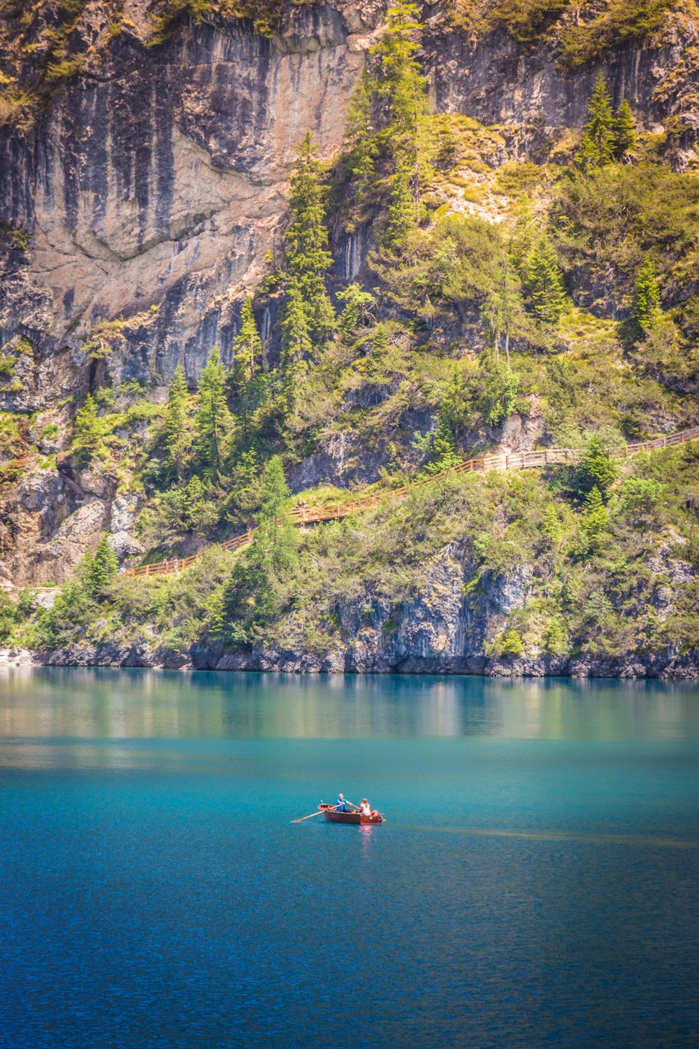a boat in the water by a cliff with trees