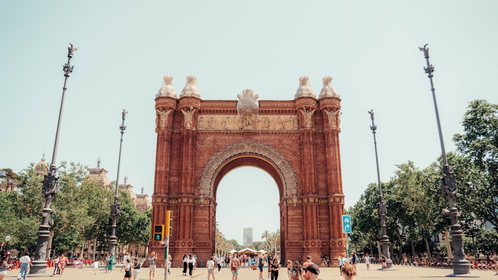 a large stone archway with people walking around with Arc de Triomf in the background