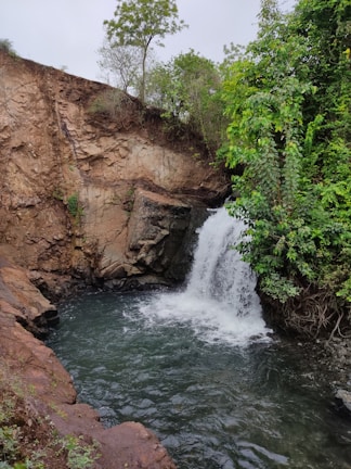 A secret waterfall cascading into a crystal-clear pool surrounded by rocks.