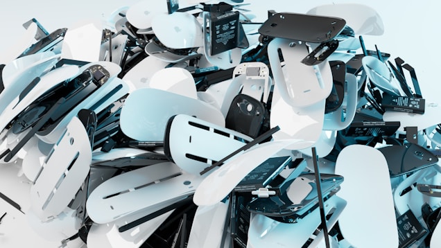 A large pile of disassembled electronic devices containing numerous circuit boards, plastic casings, and electronic components. The image features a chaotic arrangement of parts, predominantly in shades of white and black, creating a sense of clutter and randomness.