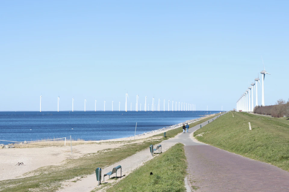 Two people walk along winding beach path lined with lush green grass and benches